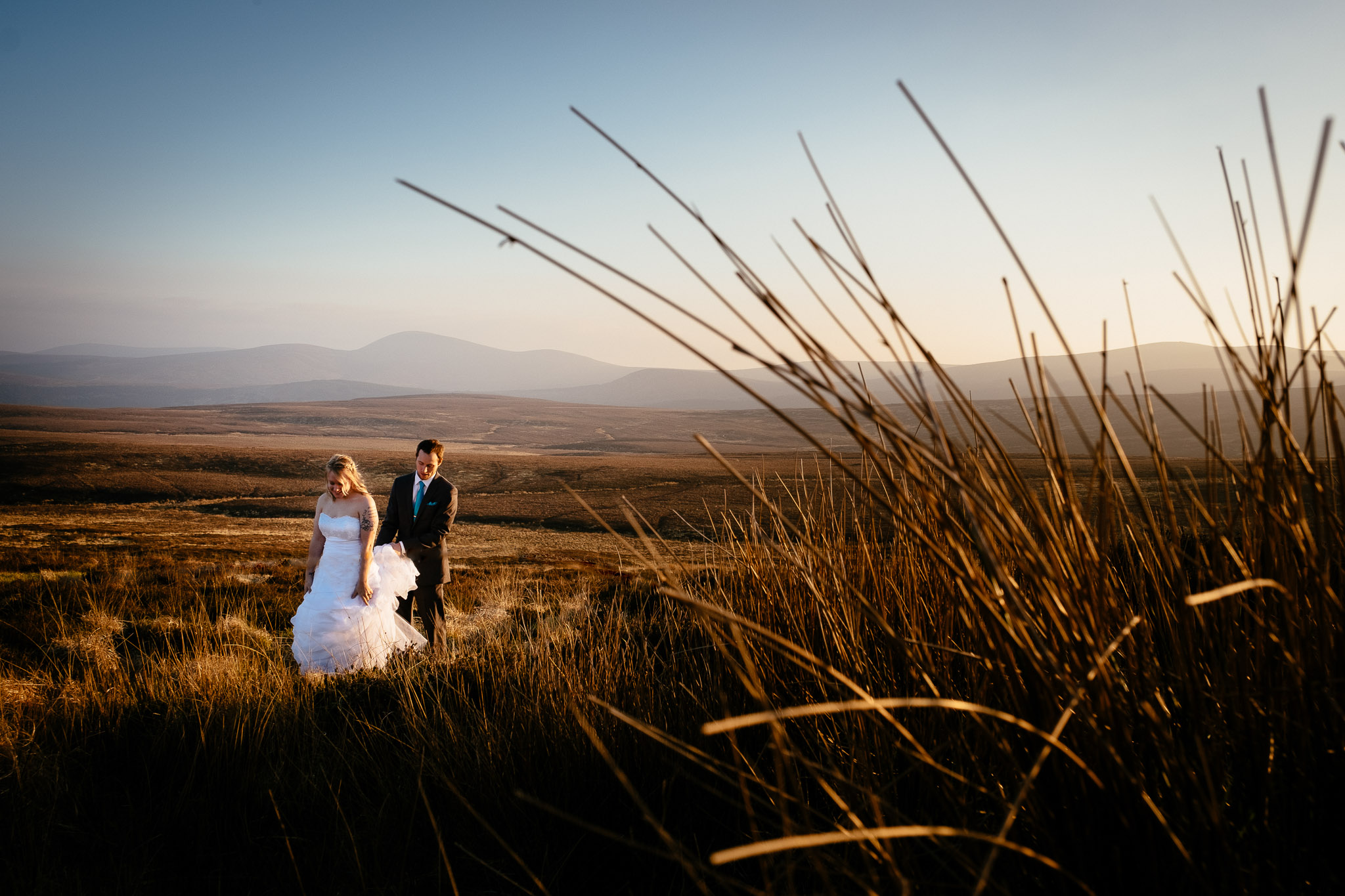 bride and groom walking through an Irish meadow at sunset