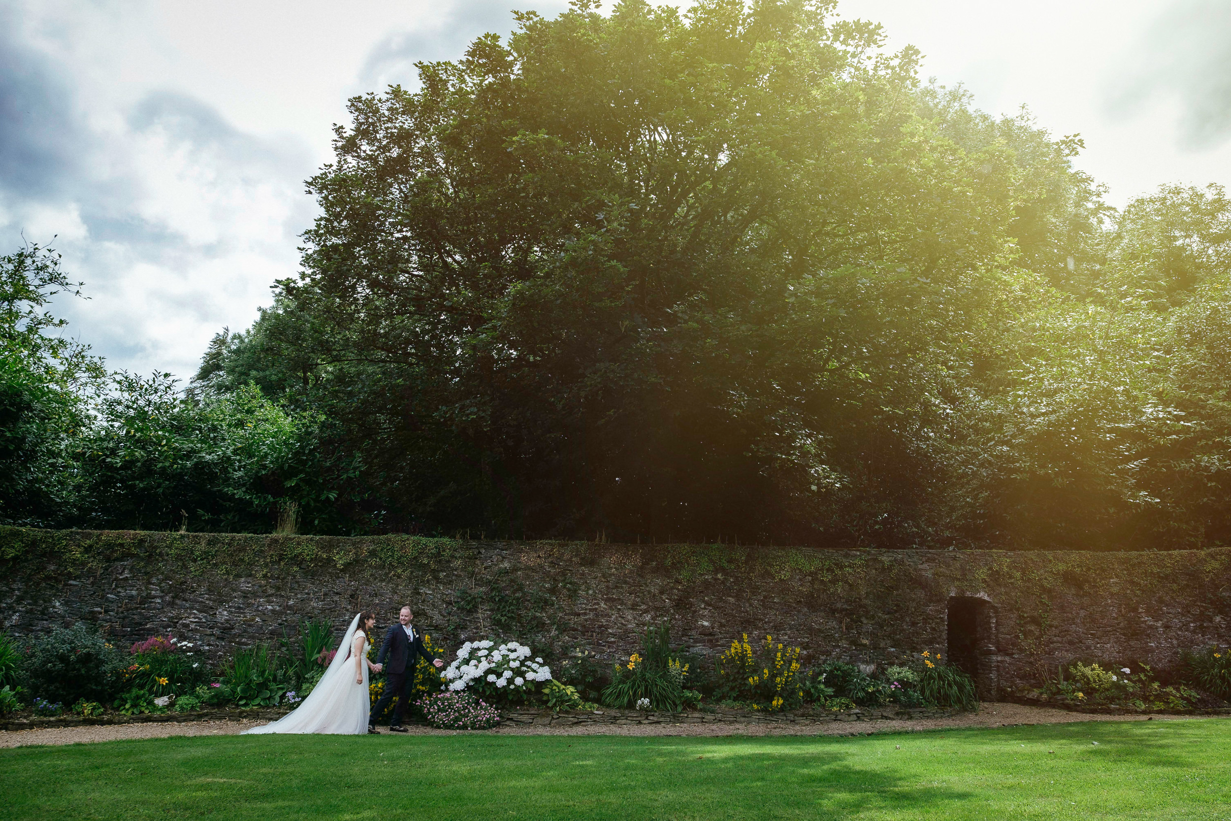 bride and groom walking in garden of ballybeg house with sunflare