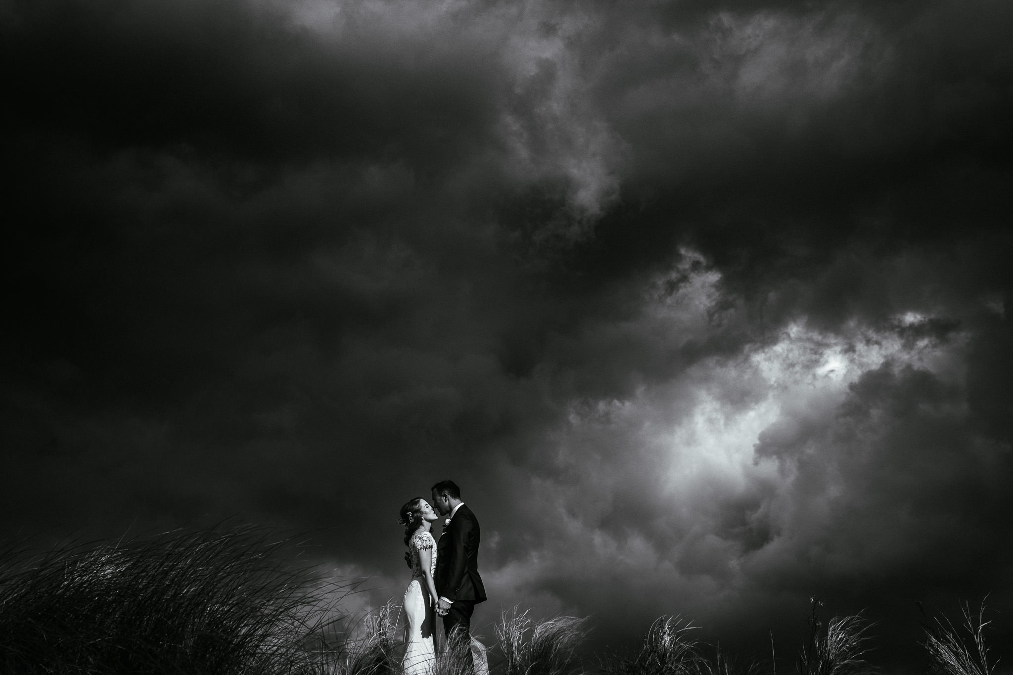 groom kissing bride on a sand dune with a dramatic stormy sky in the background at their portmarnock hotel wedding