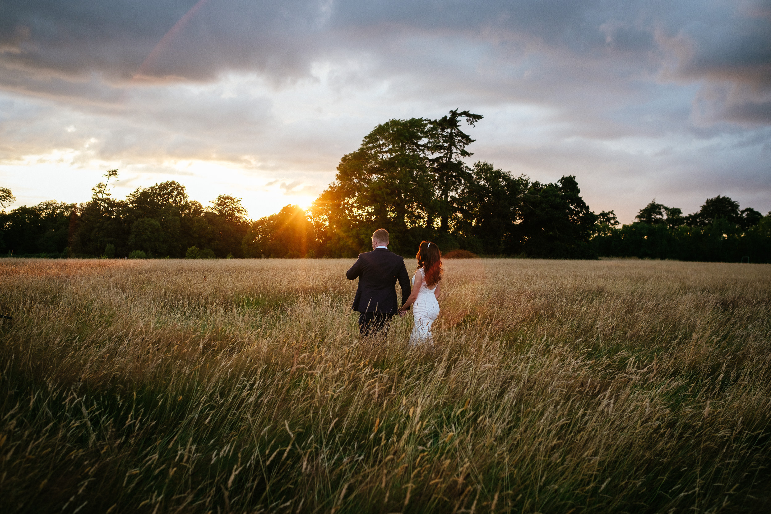 bride and groom walking through a field with an amazing sunset at their killashee house hotel wedding